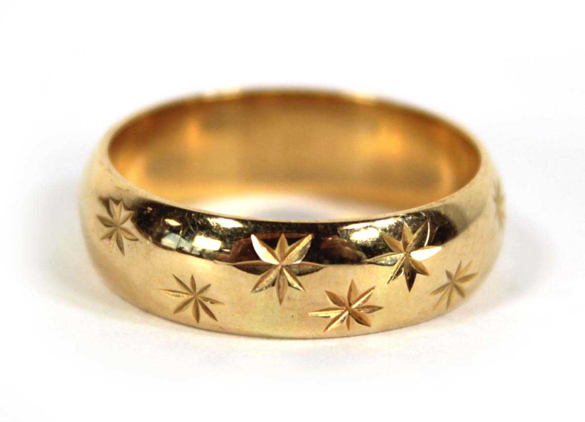 Lot 579 - An 18ct yellow gold star engraved wedding band,...